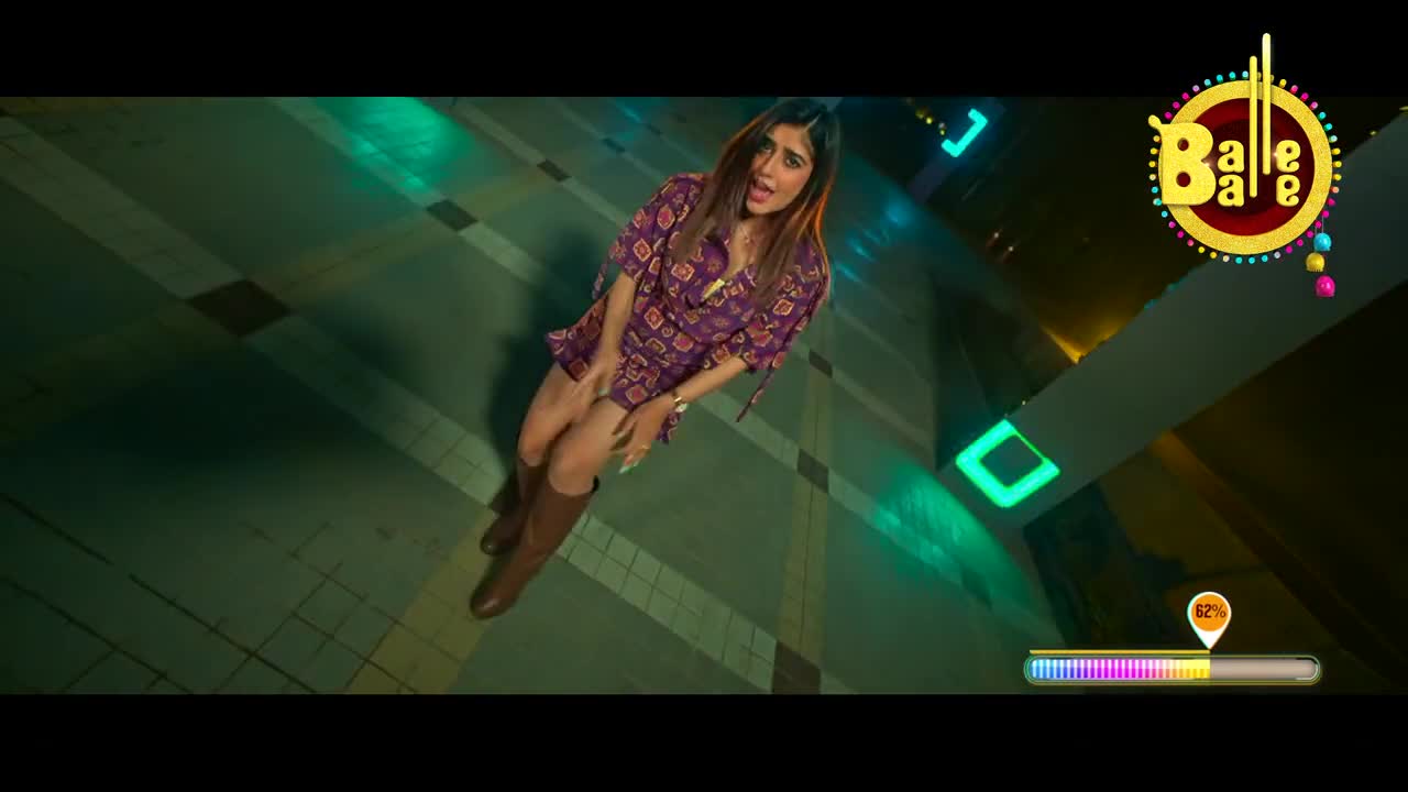 A woman in a patterned dress and tall brown boots stands in a brightly lit, geometric space. The Balle Balle logo sits in the corner as she appears to be singing.
