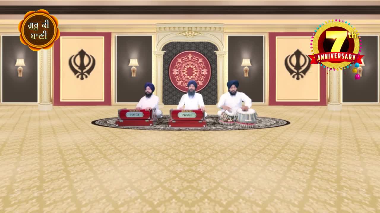 Three men in turbans sit on the floor, two playing harmoniums and one drumming on a tabla. The scene is set for a performance, with a decorative backdrop and a celebratory banner.
