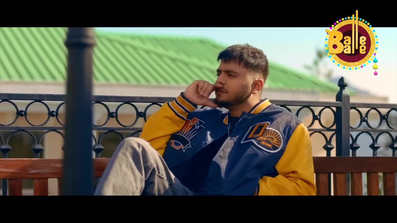 A young man in a blue and yellow letterman jacket sits on a park bench, lost in thought. The "Balle Balle" logo floats in the corner, hinting at the music video's vibe.
A young man in a blue and yellow letterman jacket sits on a park bench, lost in thought. The "Balle Balle" logo floats in the corner, hinting at the music video's vibe.