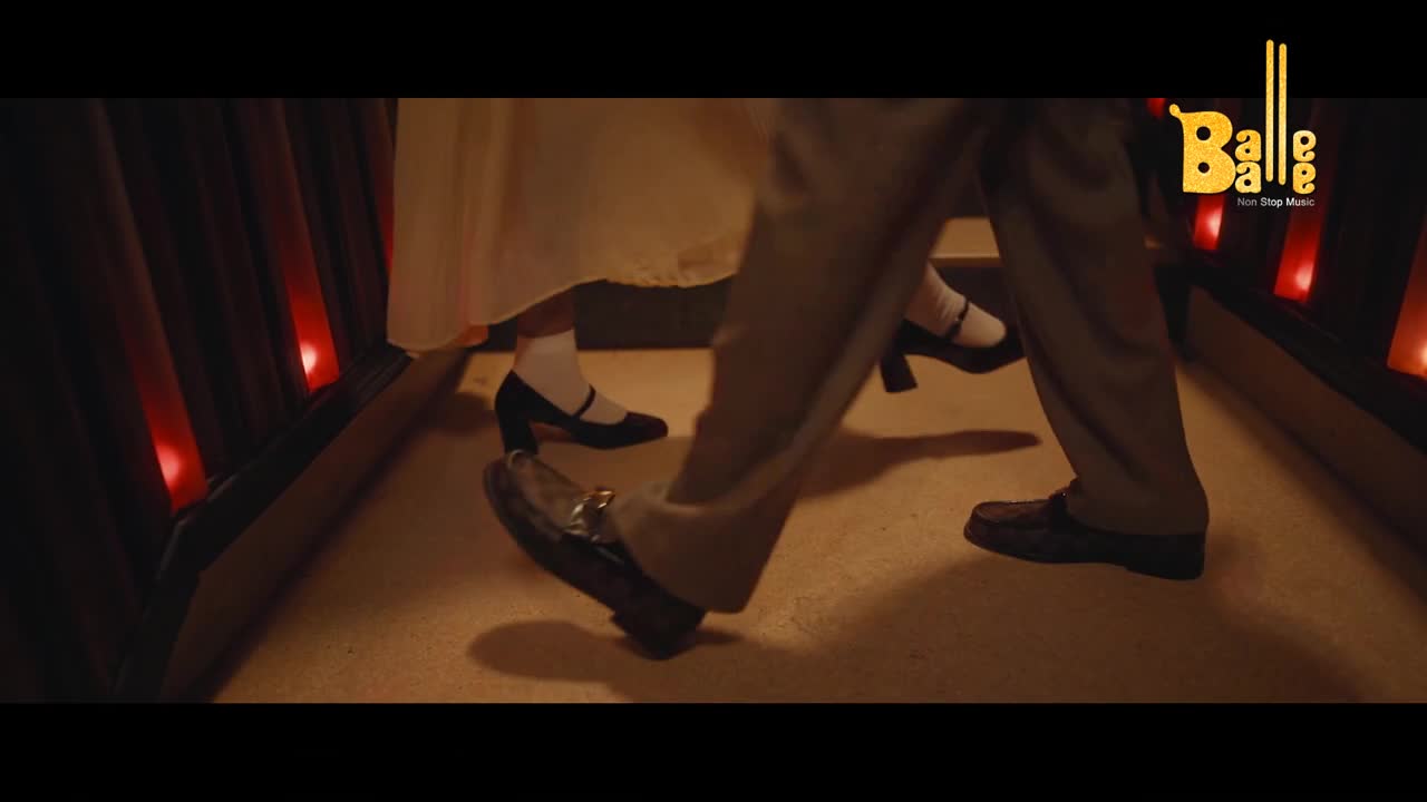 A man's shiny loafers lead the way, followed by a woman's black heels and white socks. The pair is moving forward, likely dancing to the beat of "Balle Balle."
