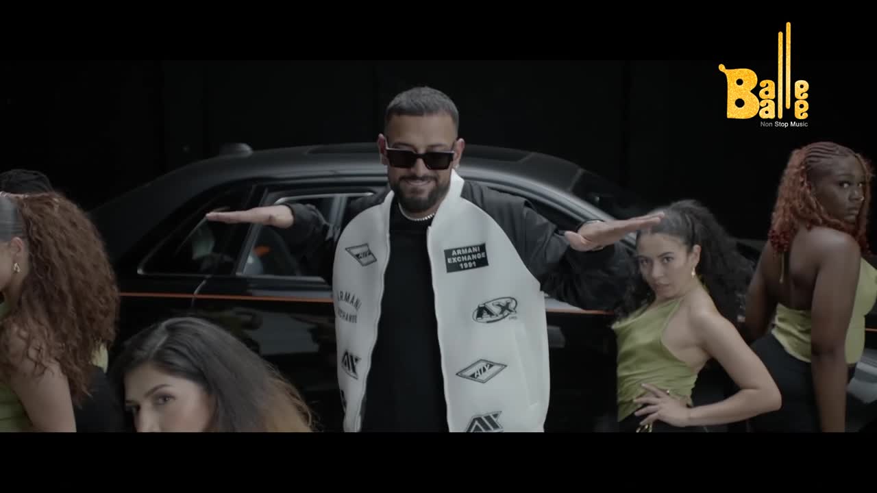 A man in sunglasses and a white jacket stands center, arms outstretched as dancers in silk tops pose around him. Behind them, a sleek black car provides a backdrop for this music video, a Balle Balle production.
