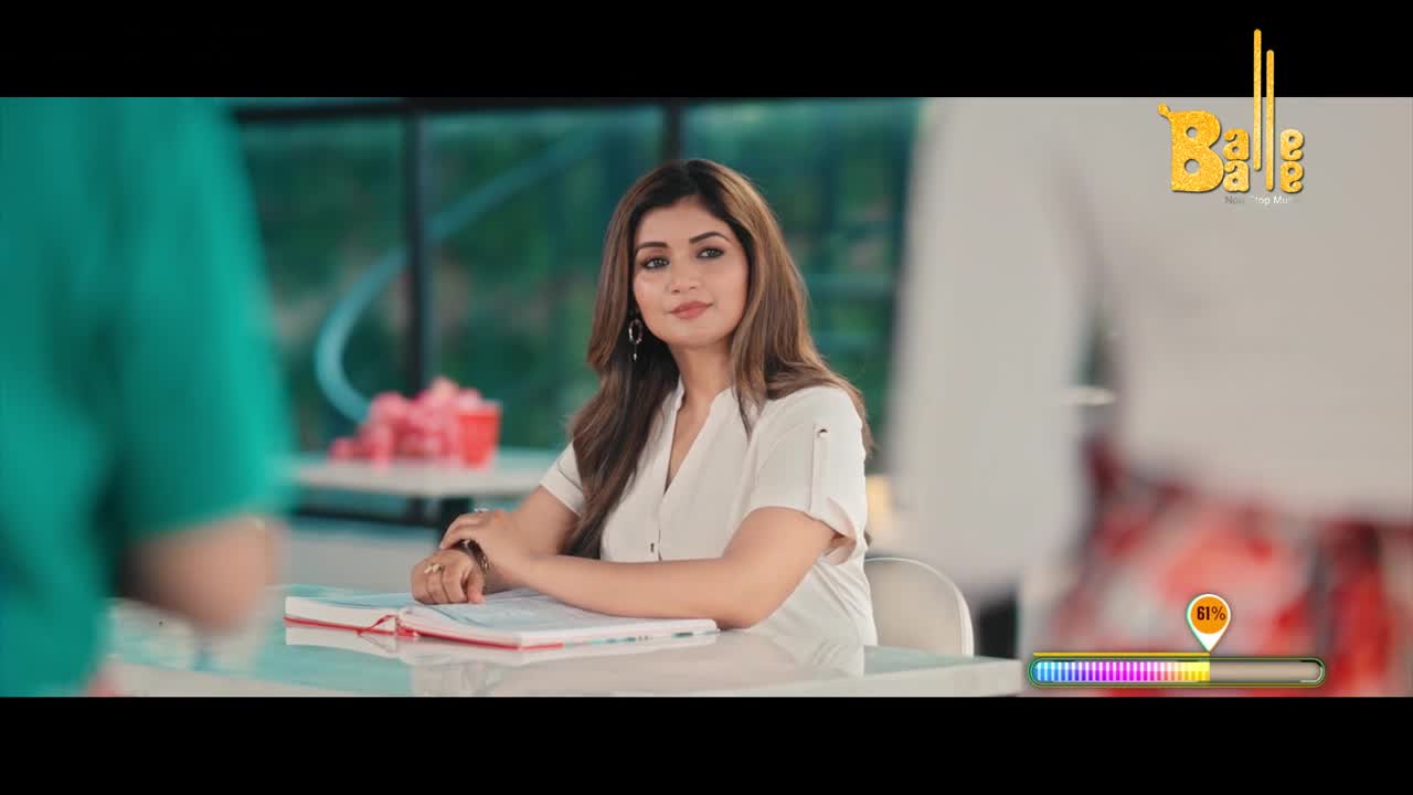 A woman in a white blouse sits at a table, looking towards someone out of frame. The "Balle Balle" logo is visible, and a progress bar indicates something is underway.
