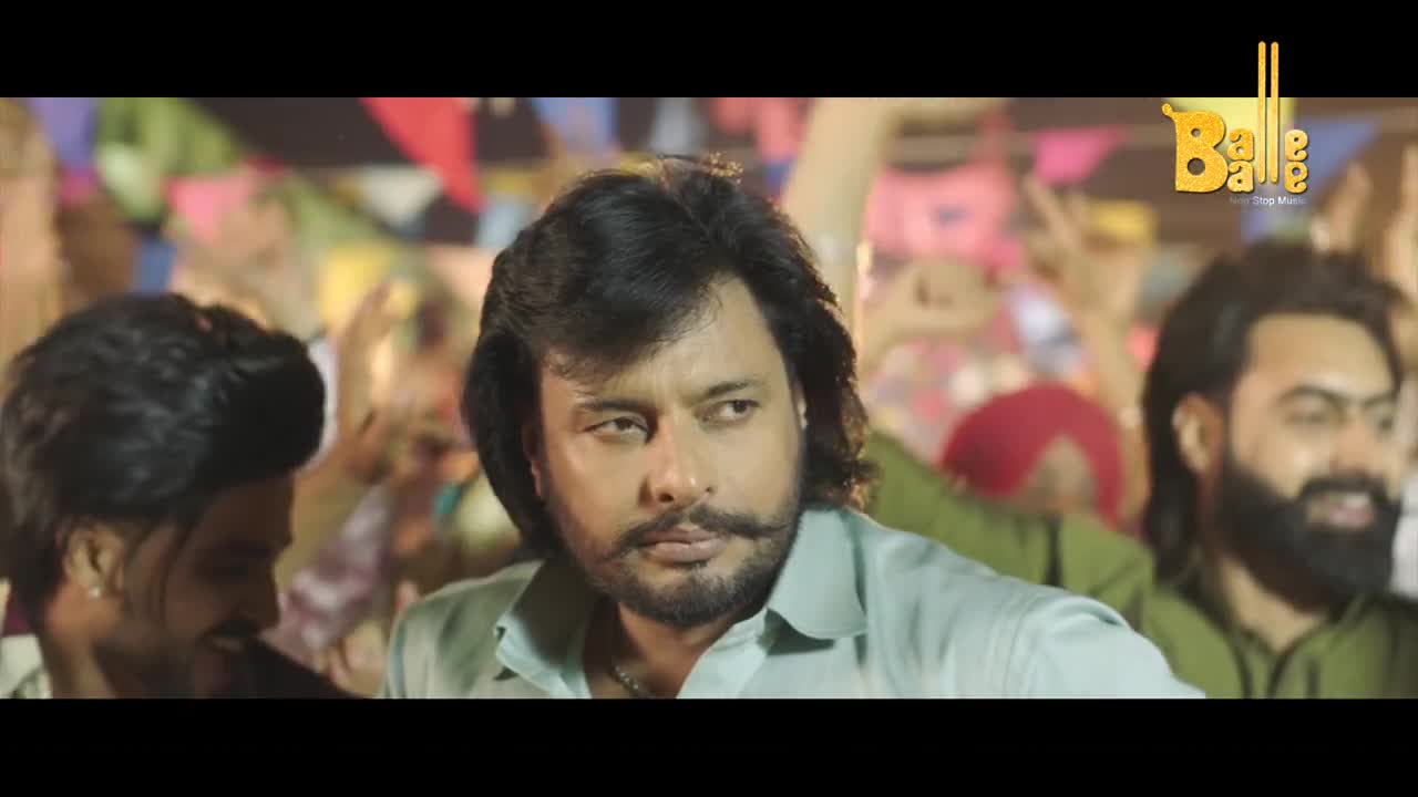 The man with the mustache stares intently, while the crowd behind him dances. The scene is brightly lit, and the logo for Balle Balle is in the corner.
