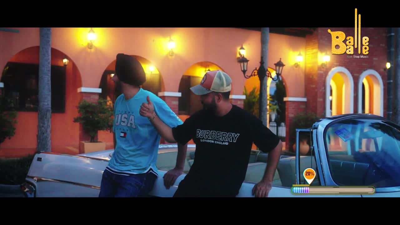 Two men lean against a vintage convertible. One, wearing a turban, gives a thumbs-up. The other sports a baseball cap and a black t-shirt.