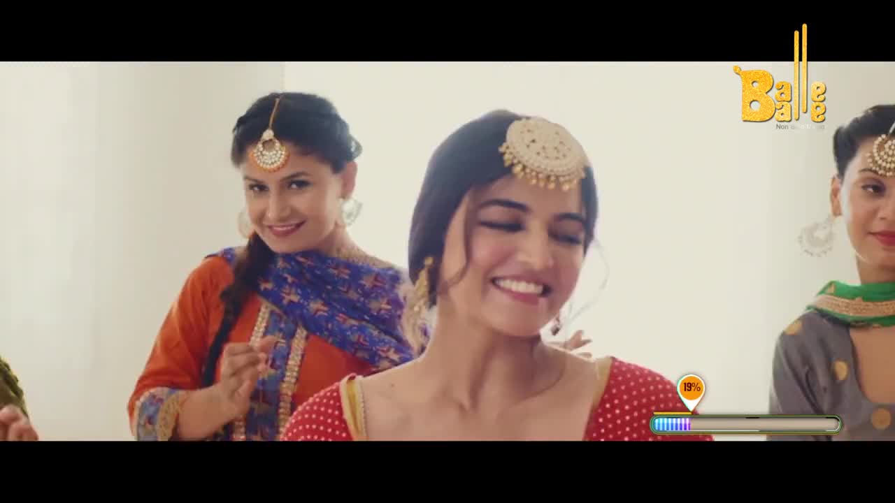 A group of women in vibrant Indian attire are gathered, their faces alight with smiles. One woman in the foreground, wearing a red and gold outfit, laughs heartily while another in an orange kurta peeks over her shoulder, a playful glint in her eyes.