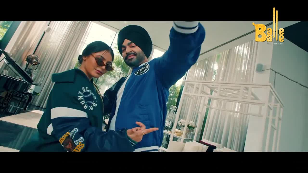A man in a blue jacket and a black turban grins, holding his arm out as if for a selfie. Beside him, a woman in a dark jacket and sunglasses leans in, her hand resting on his arm. The Balle Balle logo is visible in the corner.