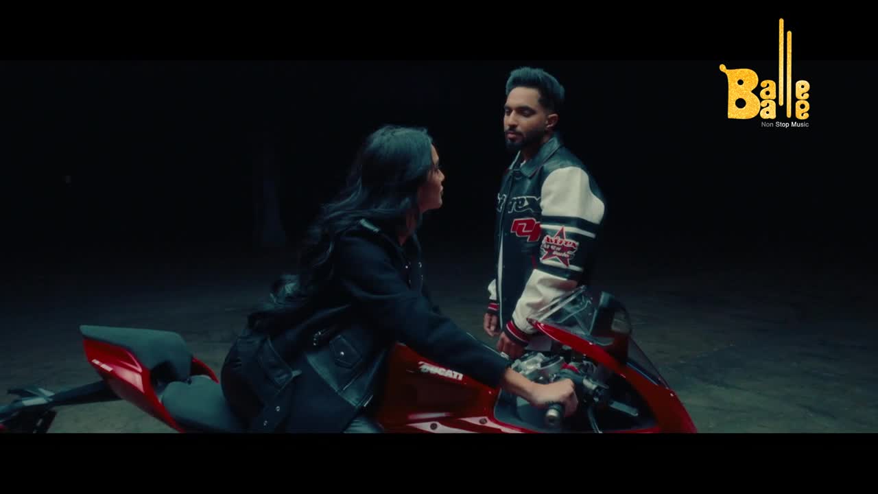 A woman in a black jacket sits on a red Ducati, her hand on the throttle. A man in a letterman jacket stands beside her, looking her in the eye. The Balle Balle logo is visible in the corner.