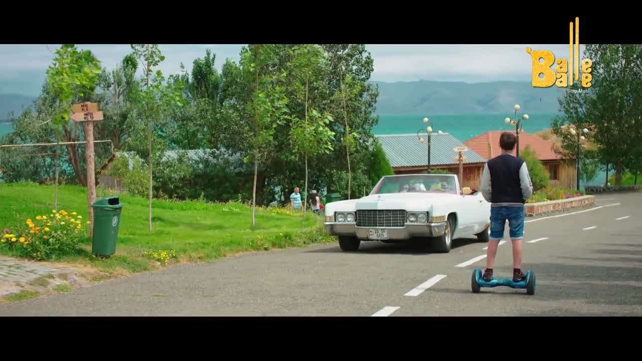 A white convertible glides down the road, its passengers visible. A young man on a hoverboard follows close behind, his attention focused ahead.