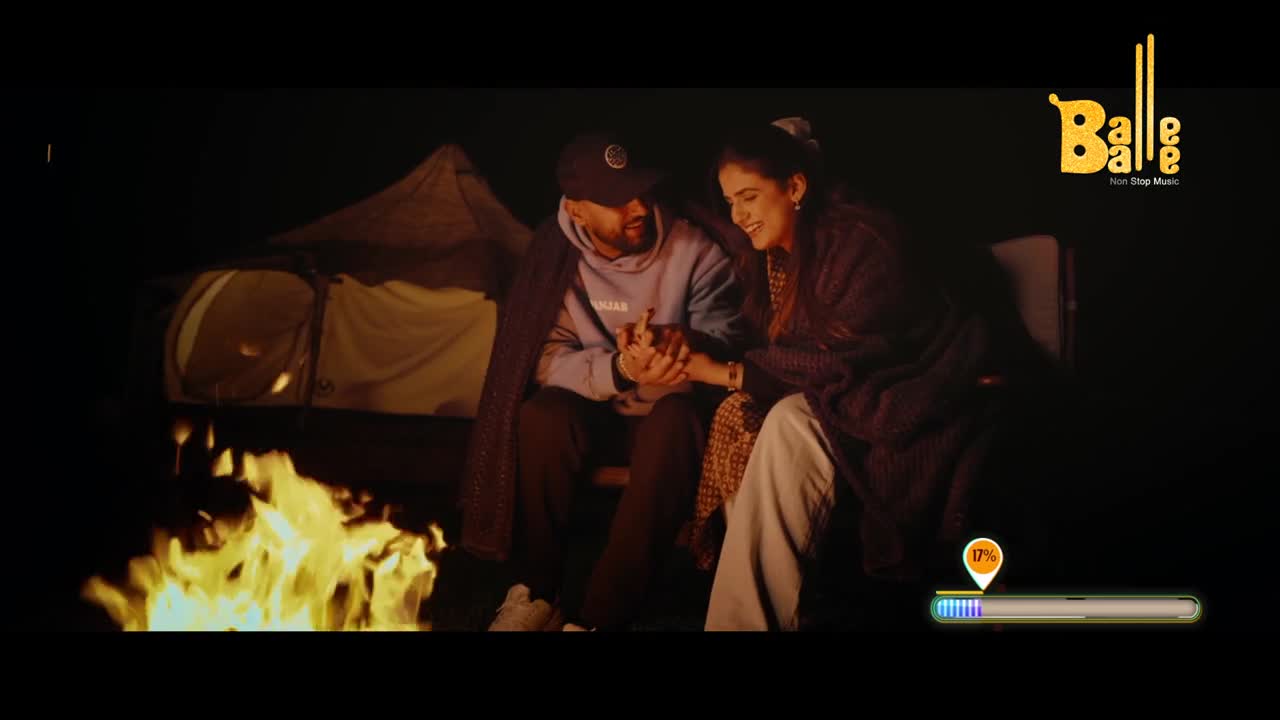 Flames leap from the campfire, warming a couple huddled together under blankets. They hold hands, their faces illuminated by the fire's glow.