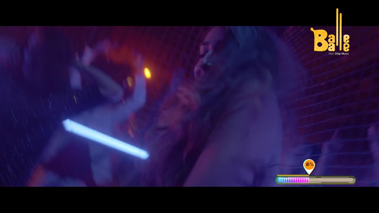 A woman with long, dark hair is captured mid-dance, her body angled as if in a powerful sway. Another figure, holding a bright blue light stick, moves in the background, their arm extended.