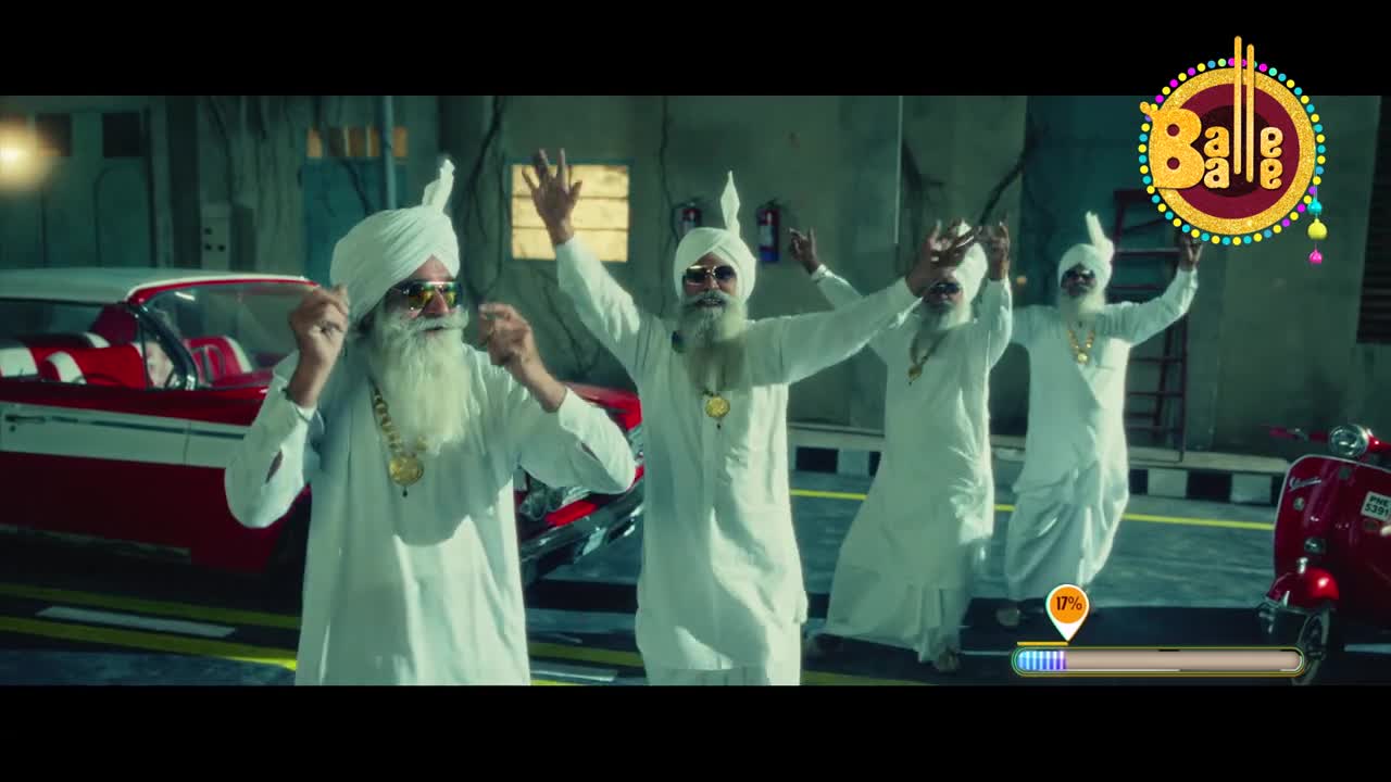 Four men in white kurtas and turbans are dancing with their arms raised. A bright red convertible and a red scooter are parked nearby.