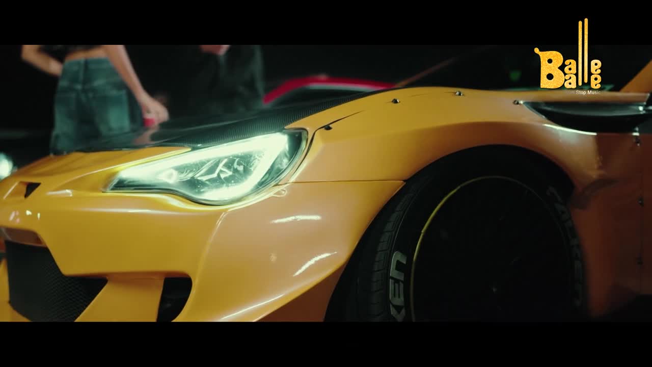 A bright yellow sports car gleams under the lights, its headlights cutting through the darkness. The "Balle Balle" logo, with its distinctive font, sits above the car, hinting at a vibrant Indian production.