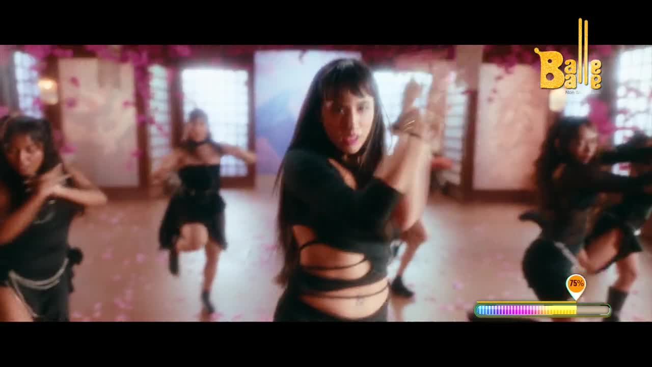 A group of women in black outfits are dancing energetically. The lead dancer in the foreground has her arms raised in a dynamic pose.