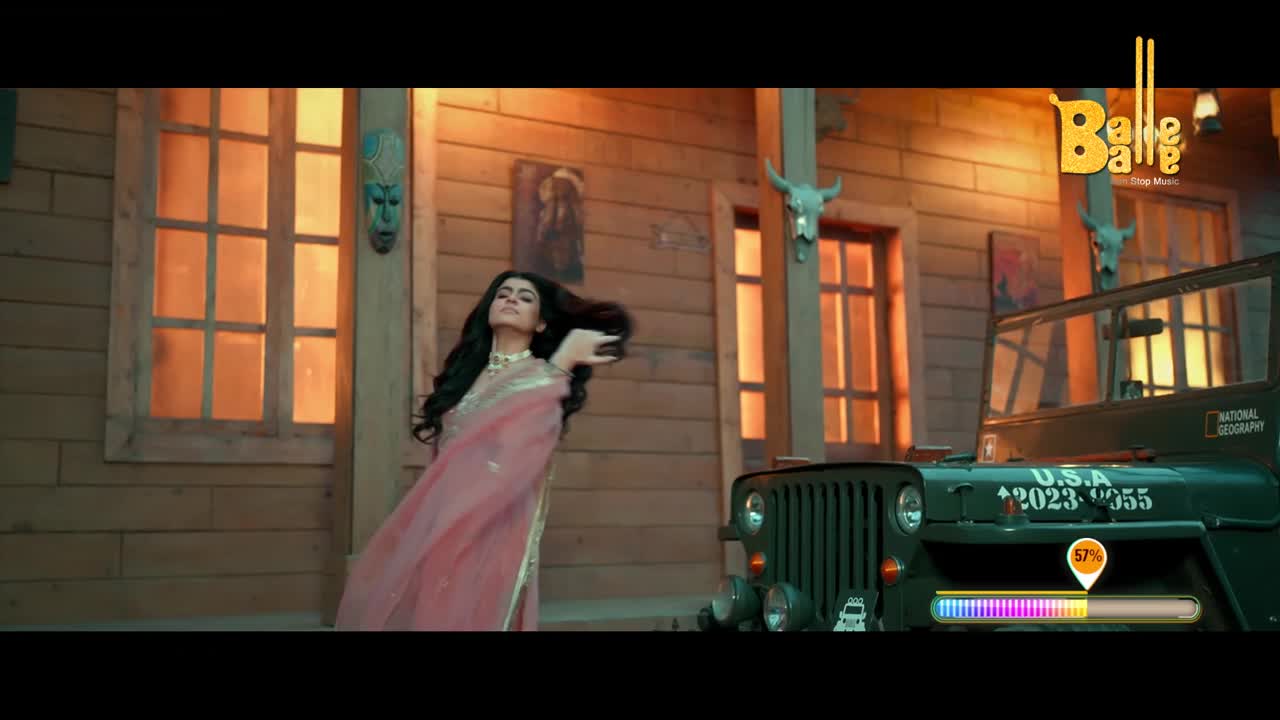 A woman in a pink sari twirls, her dark hair flying. A vintage green jeep sits parked beside a wooden building, its headlights on.