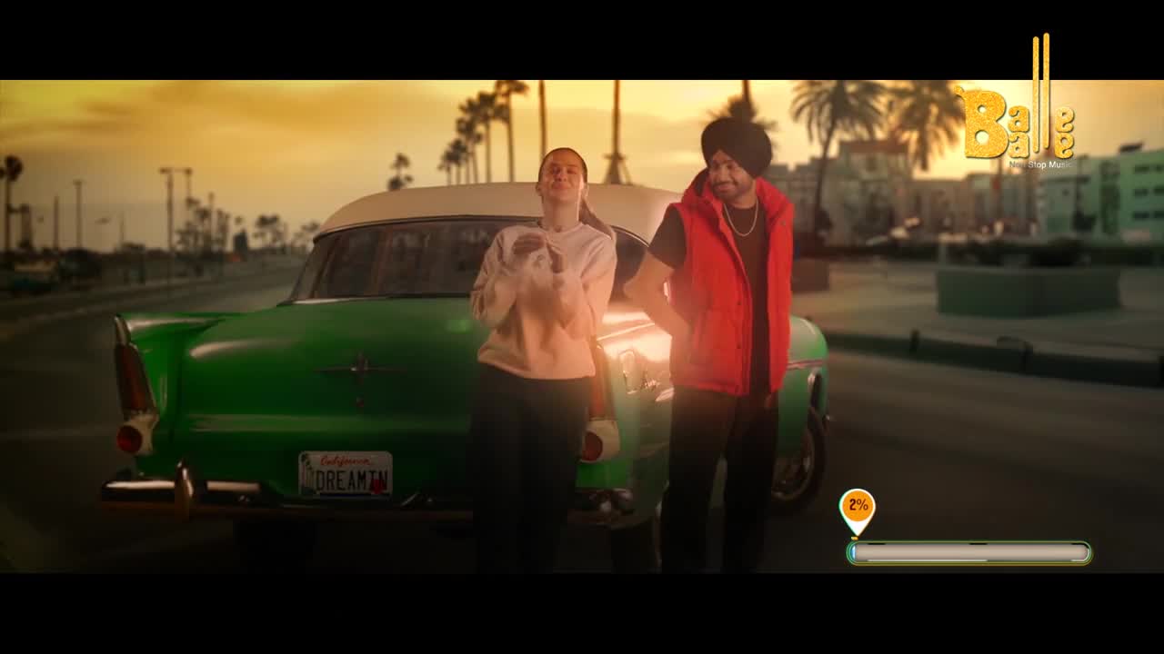 A green classic car sits parked as a young woman in a light pink hoodie and a man in a red vest and turban stand beside it. The warm, setting sun casts long shadows across the palm-lined street.