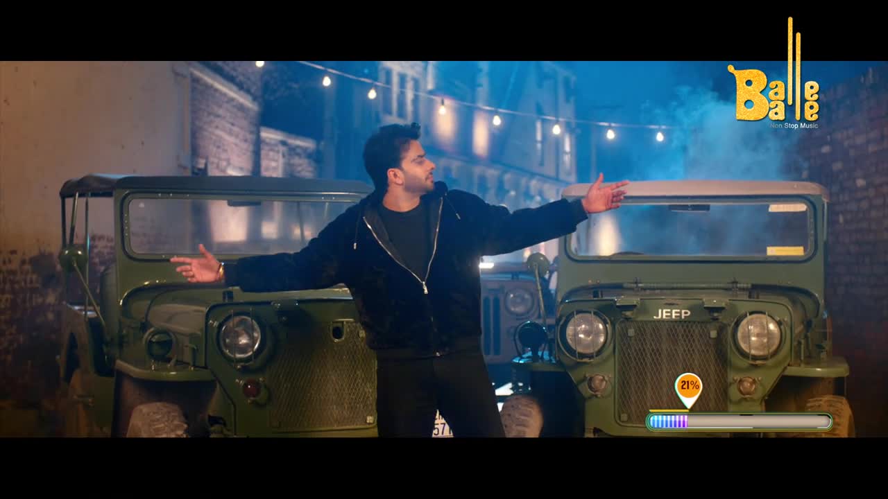 A man in a black jacket stands between two olive-green Jeeps, arms outstretched. String lights hang overhead, illuminating a brick alleyway.