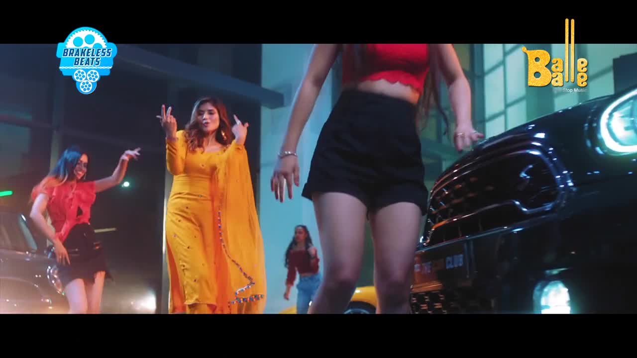 A woman in a bright yellow salwar kameez dances with her hands raised, while another woman in a red top and black shorts leans against a sleek black car. Behind them, a third woman moves to the beat in the background.