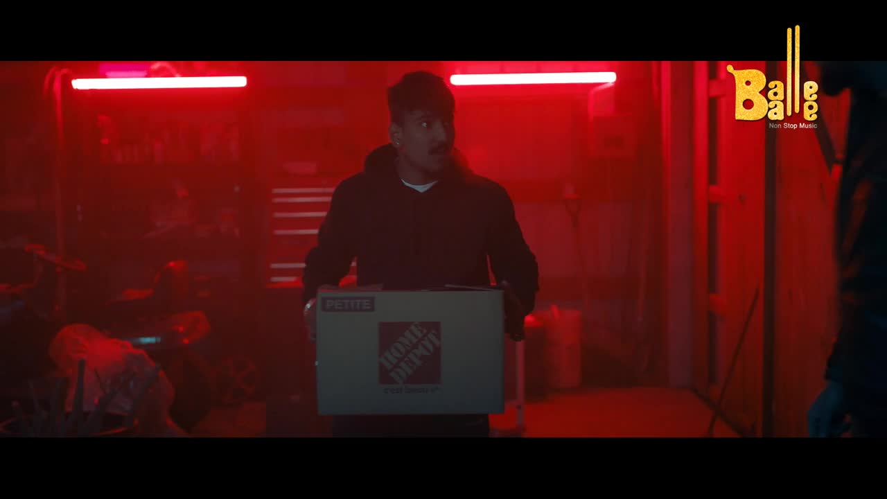 A man in a black hoodie carries a Home Depot box, his eyes wide with surprise. The room is bathed in a harsh red light, with a Balle Balle logo visible in the corner.