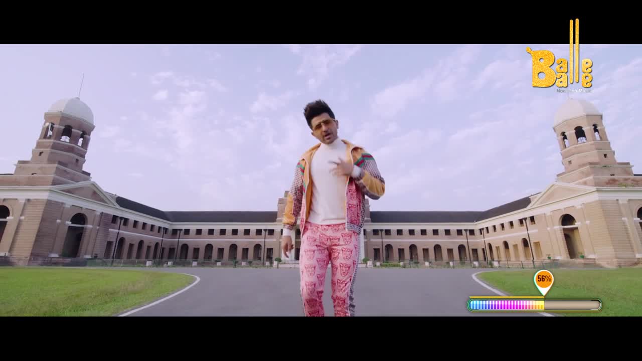 A man in bright pink pants and a patterned jacket strides forward on a paved path. He's in front of a grand, tan building with two prominent towers under a pale sky.