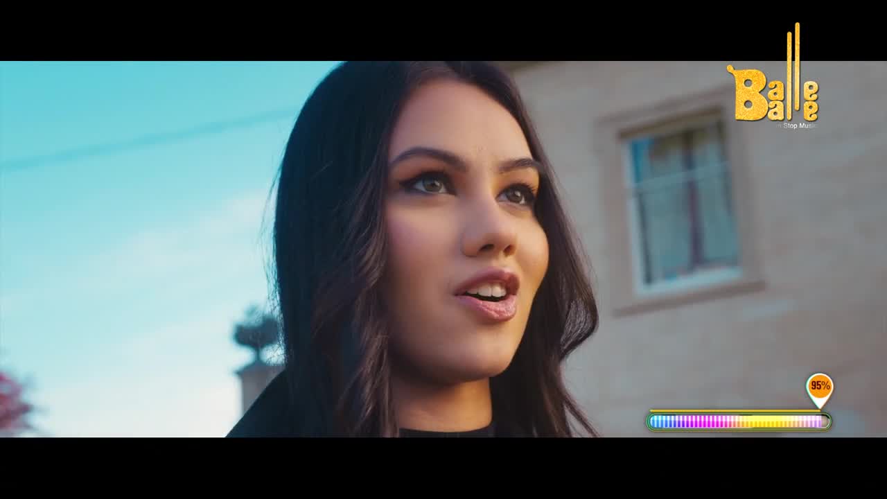 A young woman with dark hair turns her head, her mouth slightly open as if speaking. The bright Indian sun illuminates her face against a backdrop of a pale building.
