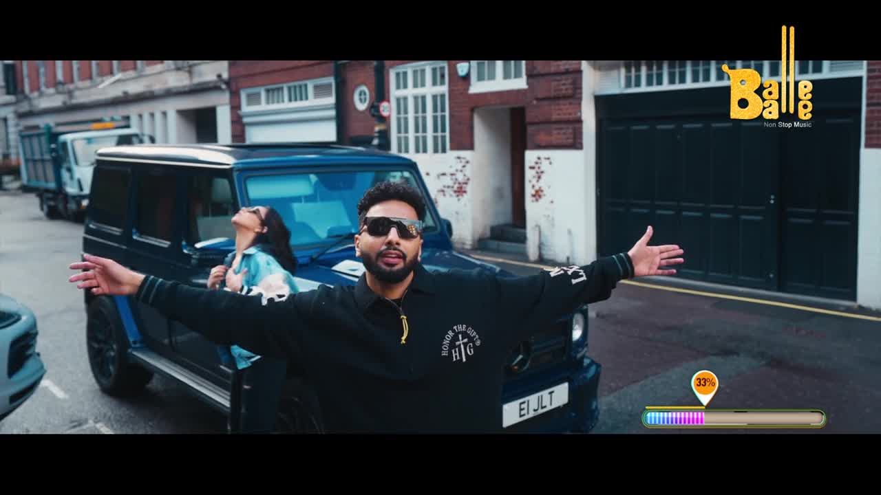 A man with his arms outstretched stands before a dark blue SUV. A woman leans out the passenger window behind him, looking up. The Balle Balle logo appears in the upper right corner.