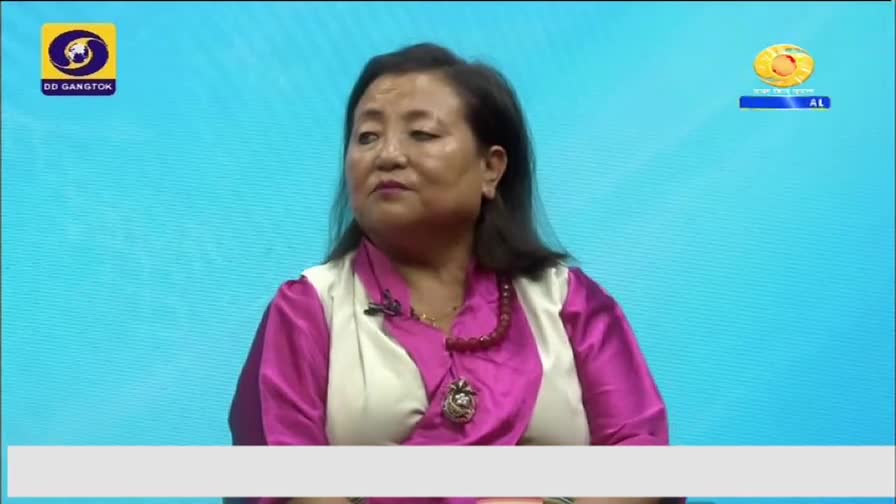 A woman in a pink and white top sits in front of a blue backdrop, likely on a DD Arun Prabha broadcast. The logos for DD Gangtok and the network are visible in the corners.
