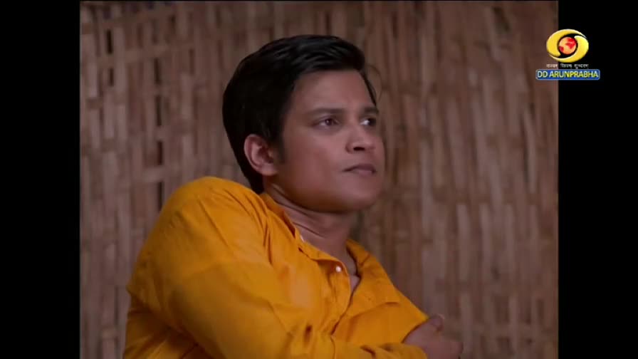 The person in the yellow shirt is looking off to the side, their expression serious. The DD Arun Prabha logo sits in the corner, suggesting a broadcast from India.
