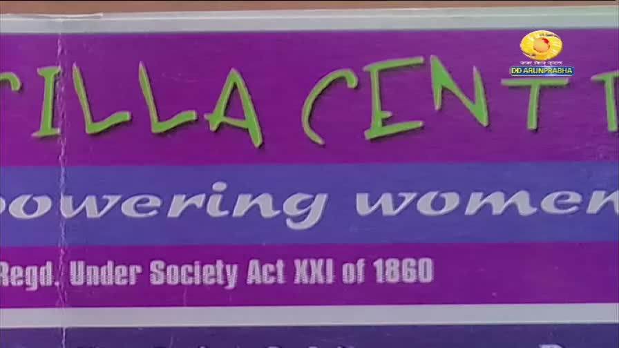 The words "TILLA CENTRE" in green script stand out against a purple background. Below, the phrase "powering women" is visible, with the DD Arun Prabha logo in the corner.
