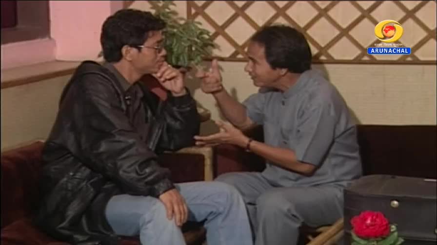 Two men are talking on a couch. One gestures with his hands while the other listens intently. The DD Arun Prabha logo is visible in the background. Two men are talking on a couch. One gestures with his hands while the other listens intently. The DD Arun Prabha logo is visible in the background.