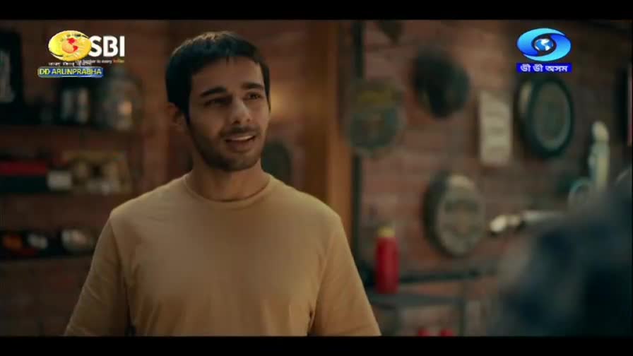 A young man in a tan t-shirt smiles as he speaks, his eyes directed off-camera. The DD Arun Prabha logo appears in the upper left corner, beside the SBI logo.