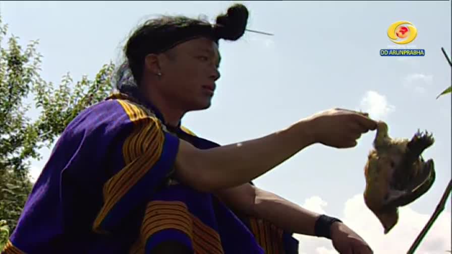 A person in traditional Indian attire holds a small, lifeless bird. The DD Arun Prabha logo is visible in the corner.