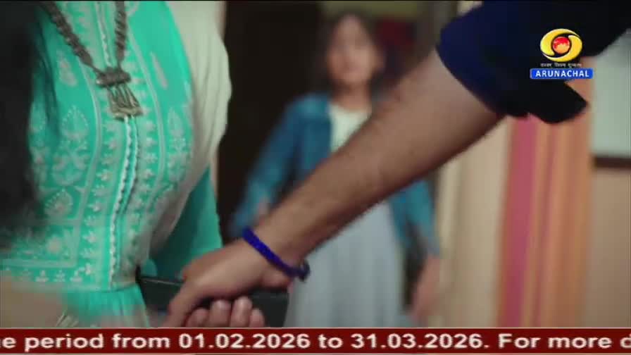 A hand, adorned with a blue beaded bracelet, reaches out to grasp something near a woman in a turquoise salwar kameez. In the background, a young girl stands, her form slightly blurred.