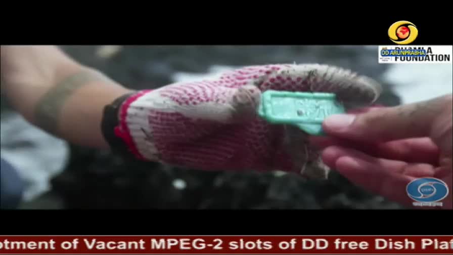 A gloved hand holds out a small, turquoise tag. Another hand reaches to take it. The DD Arun Prabha Foundation logo is visible in the corner.