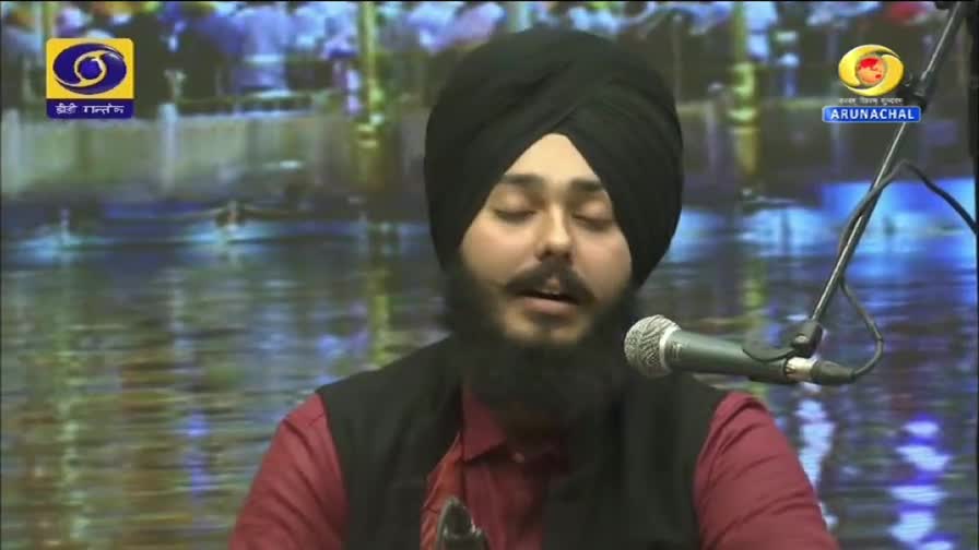 A man with a black turban and beard sings into a microphone, his eyes closed. The DD Arun Prabha logo appears on screen, indicating a broadcast from India.