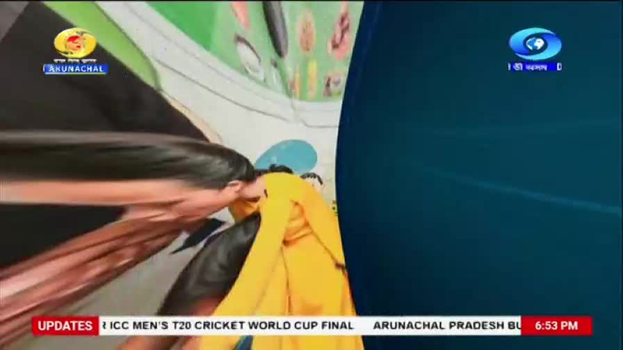 A person in a yellow garment leans forward, their face obscured. The DD Arun Prabha logo is visible in the upper left corner.