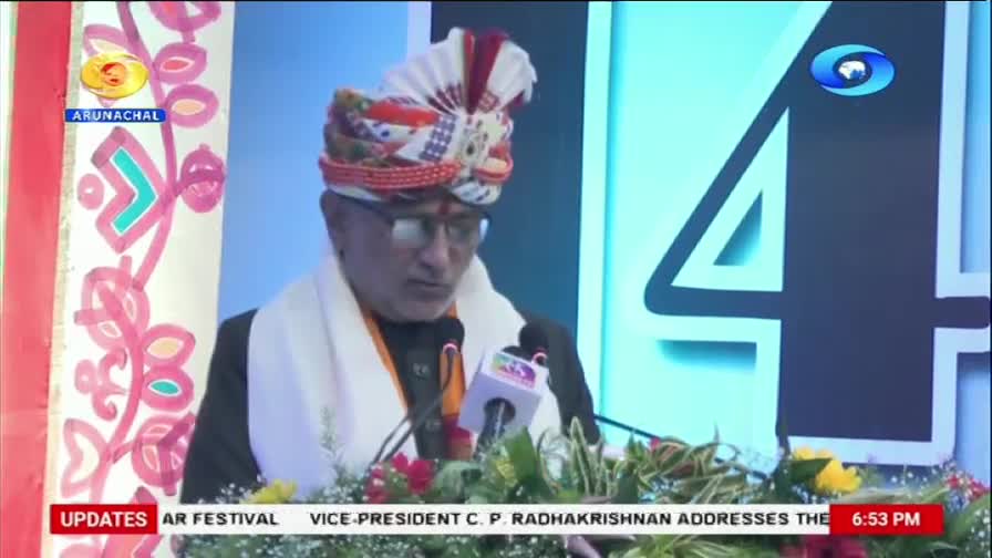 The Vice-President, wearing a vibrant turban, addresses the crowd from behind a podium adorned with flowers. A large, stylized "4" dominates the background, with the DD Arun Prabha logo visible.