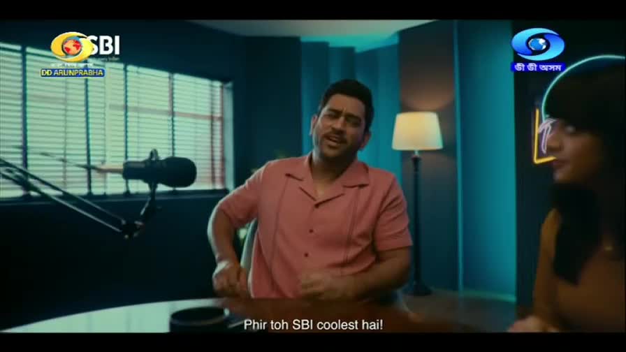 A man in a pink shirt leans forward, gesturing as he speaks into a microphone. Beside him, a woman with bangs listens intently. The DD Arun Prabha logo is visible in the corner.