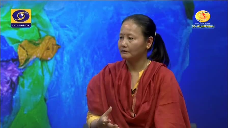 A woman in a red shawl speaks, her hands gesturing. The DD Arun Prabha logo appears on screen.