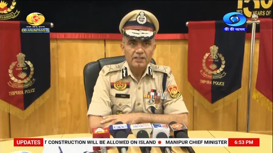 A police officer in uniform speaks into multiple microphones. Behind him, banners display the Tripura Police insignia and the DD Arun Prabha logo.