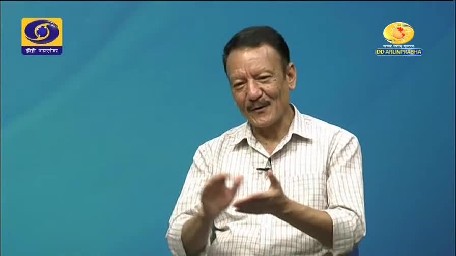 A man with a mustache smiles and gestures with his hands. The DD Arun Prabha logo appears on the screen.