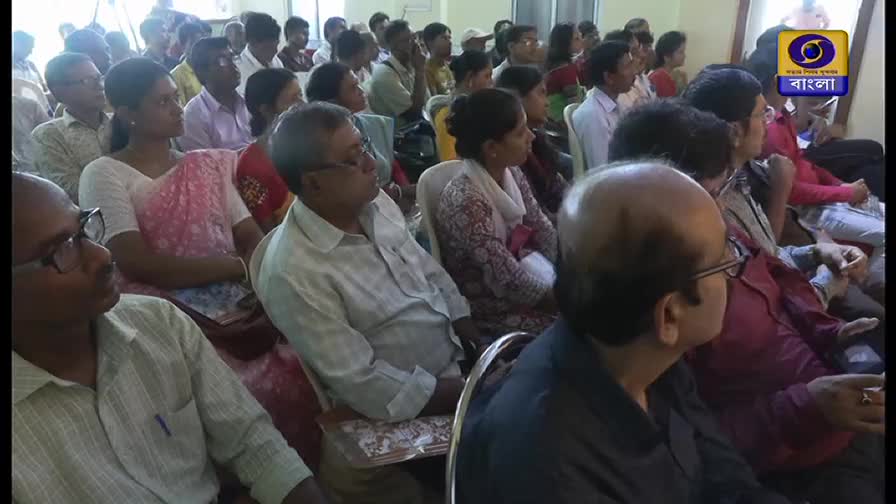 A large group of people, mostly wearing glasses, are seated and looking towards the same direction. The DD Bangla logo is visible in the corner, suggesting this is a televised event in India.

