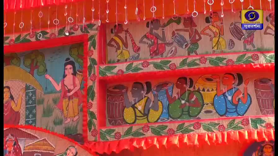 Painted figures in traditional attire are depicted on the decorative panels, with musicians playing drums and wind instruments. The DD Bangla logo is visible, suggesting this is part of a broadcast from India.
