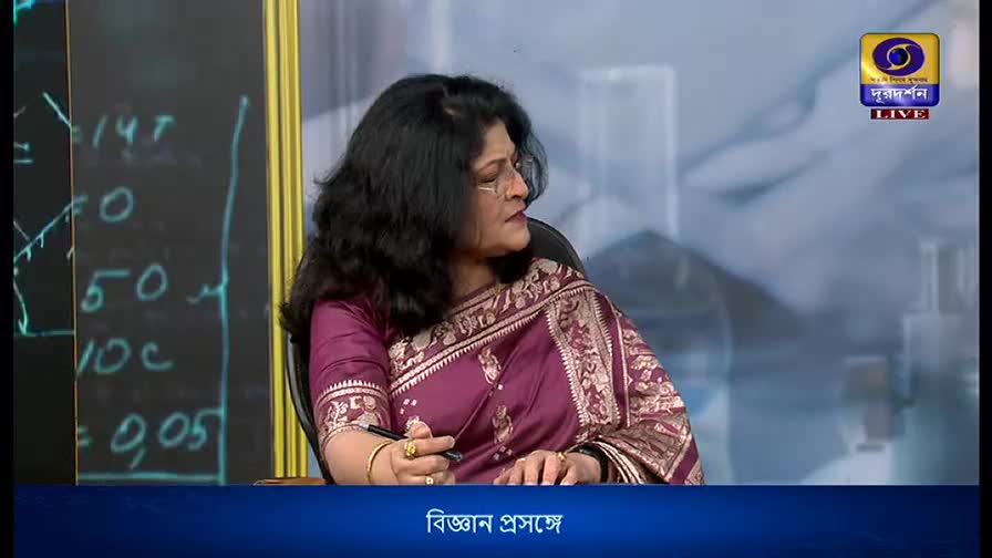 A woman in a maroon sari sits at a desk, looking intently to her right. The DD Bangla logo is visible in the corner, and the bottom of the screen reads "Bigyan Prasange."
A woman in a maroon sari sits at a desk, looking intently to her right. The DD Bangla logo is visible in the corner, and the bottom of the screen reads "Bigyan Prasange."