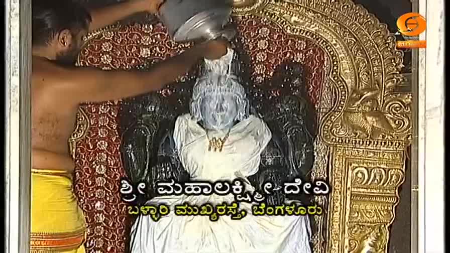 A person pours a milky liquid over a statue of a deity. The liquid cascades down the dark figure, creating a white stream.
