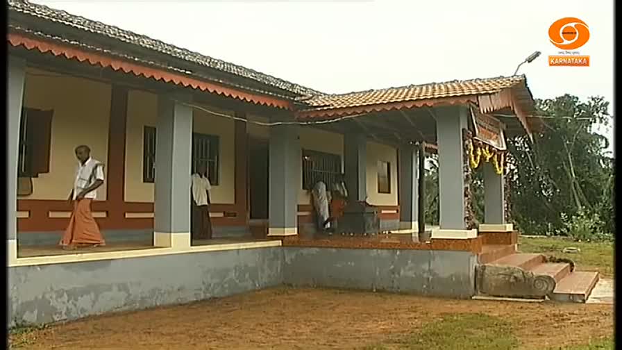 Men in traditional clothing walk along the veranda of a building with a tiled roof, while others gather near a window. The logo for DD Chandana, a Kannada-language television channel, is visible in the corner.
