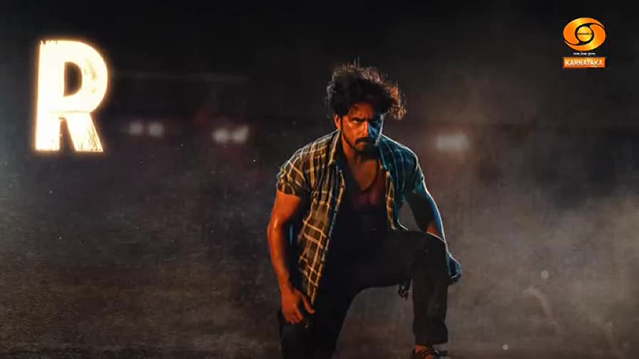 A man in a plaid shirt kneels, looking intense, with a large glowing "R" behind him.  The DD Chandana logo is visible in the corner, suggesting a scene from a show.
