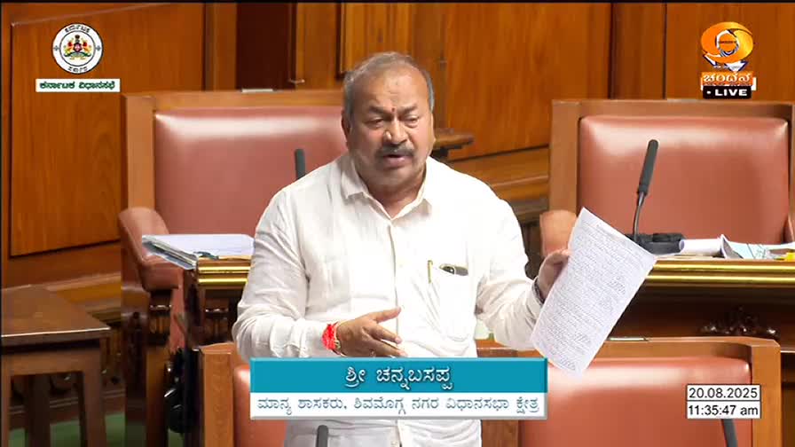 A man in a white shirt gestures with his left hand while holding a sheaf of papers in his right. The DD Chandana logo is visible, and the date and time are displayed on the screen.
