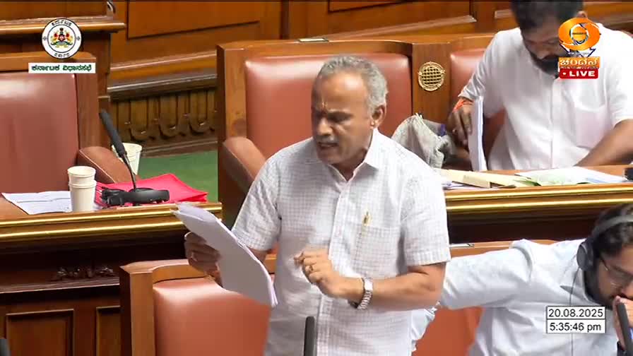 A man in a light-colored shirt gestures with papers, speaking into a microphone. The scene is being broadcast live on DD Chandana, with the date and time displayed in the corner.
