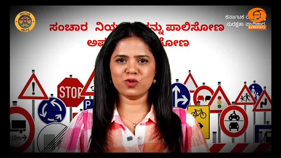 A woman with dark hair and a pink shirt speaks directly to the camera, framed by a backdrop of road signs. The set appears to be from a DD Chandana program, likely discussing traffic safety in Karnataka, India.
