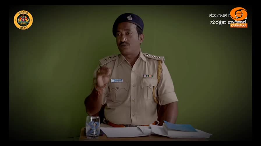 A uniformed police officer gestures with his right hand, speaking directly to the camera. Behind him, the DD Chandana logo and a Karnataka government logo are visible.
